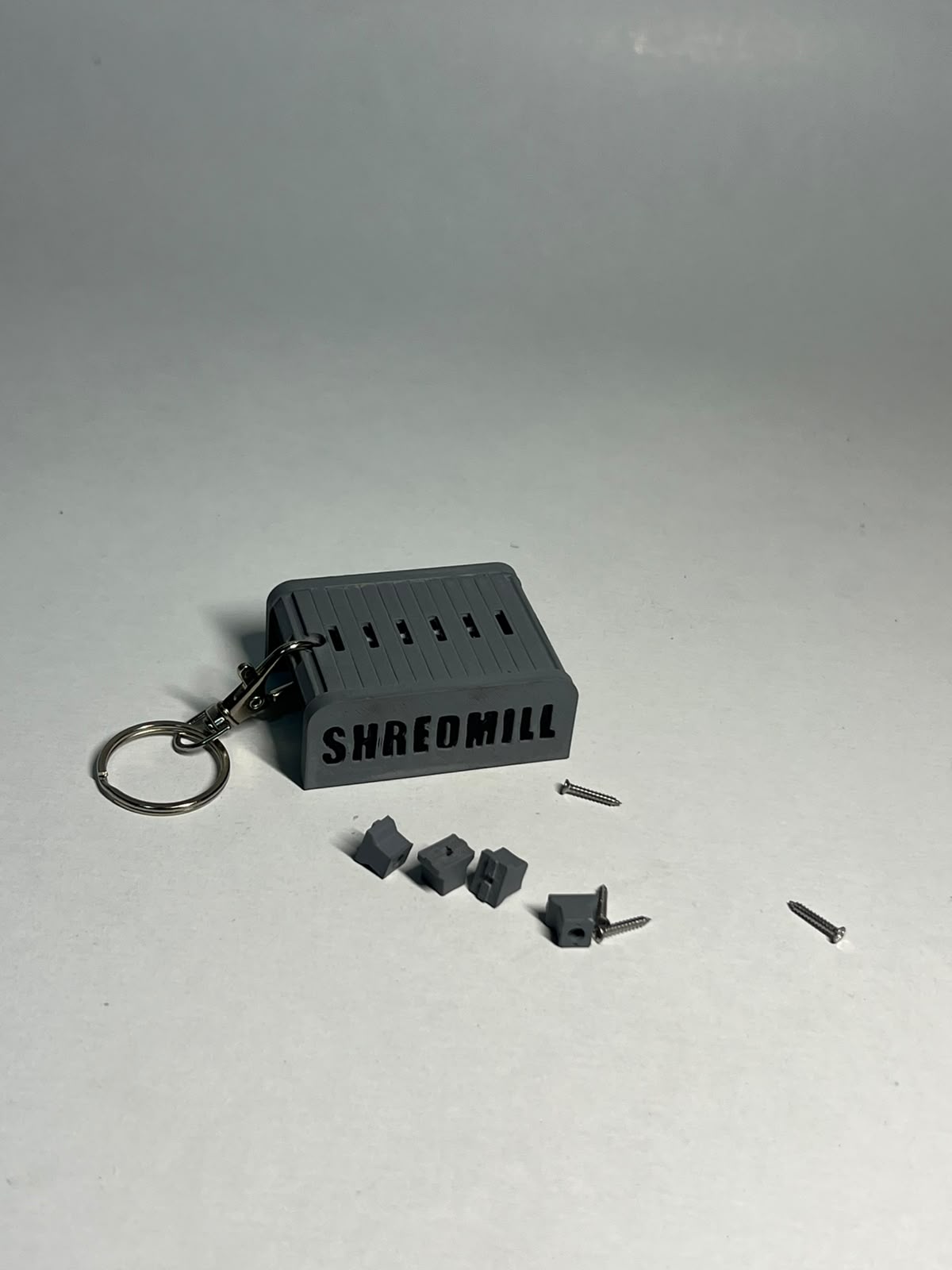 Shredmill keychain with its ring and small gray components on a table